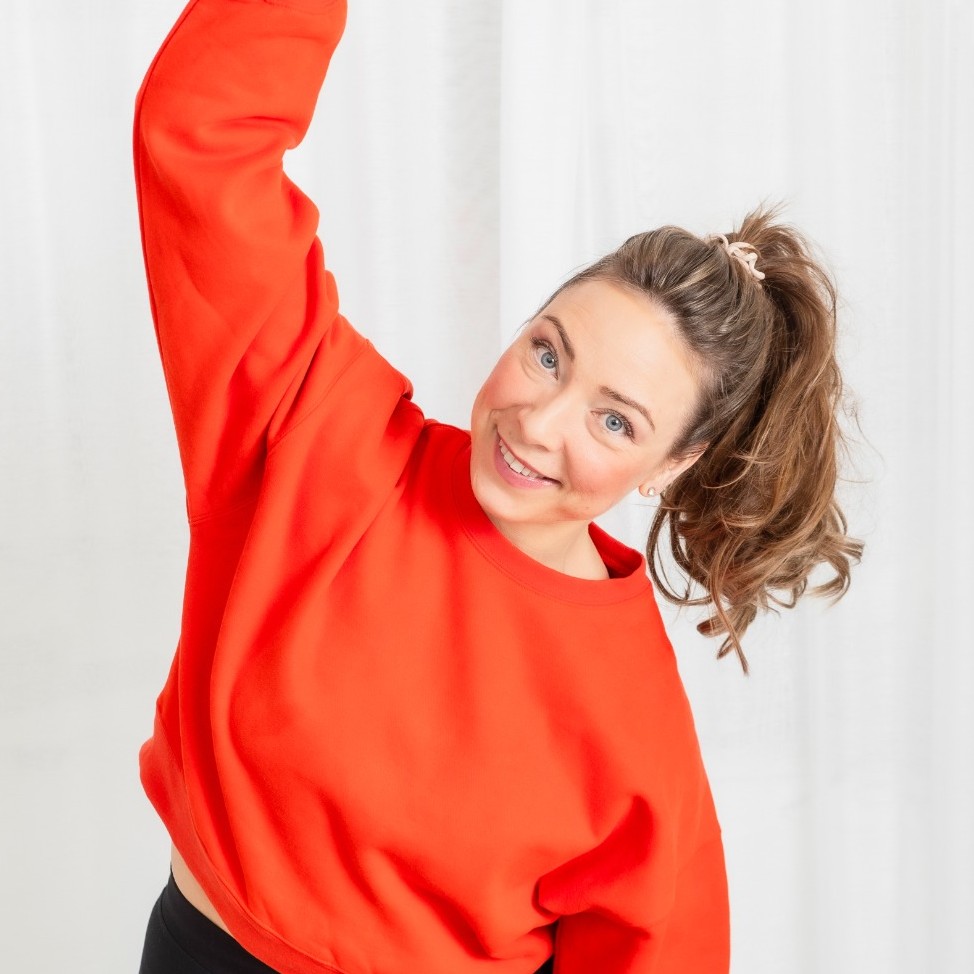 Ilona Siitonen psykofyysinen fysioterapeutti hymyilee kirkkaan punaisessa paidassa venytellen